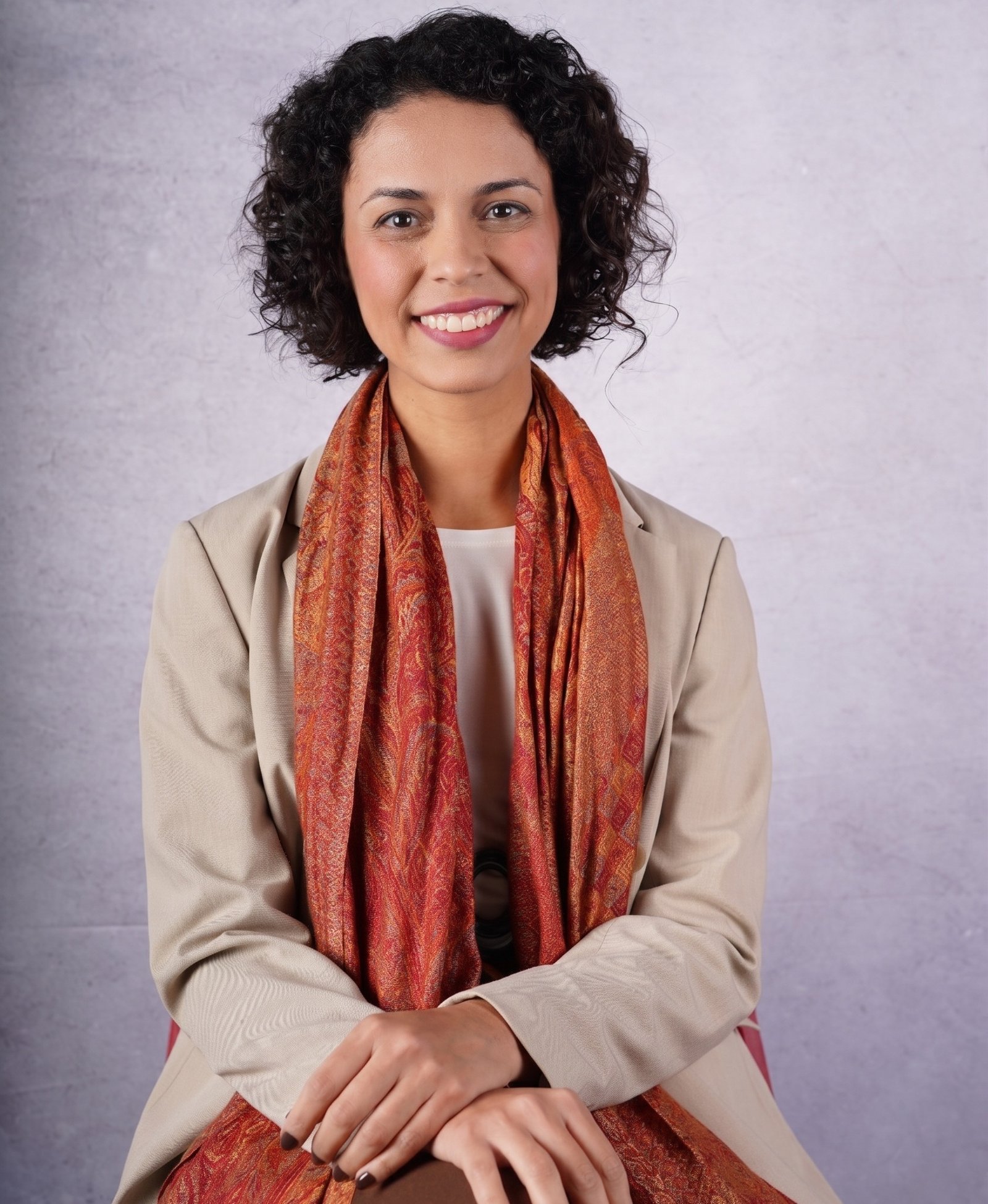 Retrato de Jéssica Freitas, sorrindo, usando blazer bege, echarpe terracota e colar verde